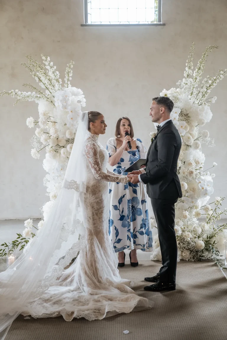 Bride and groom exchanging vows under stunning white floral arch with wedding celebrant Charis White